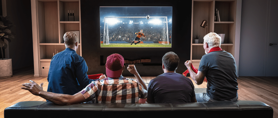 Παρέα παρακολουθεί ποδοσφαιρικό αγώνα σε καθιστικό δωμάτιο σπιτιού.